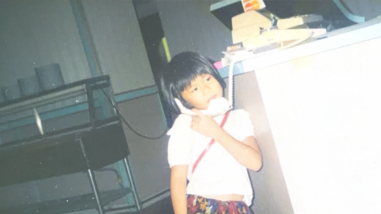 A young girl cradles a landline phone in a restaurant. 