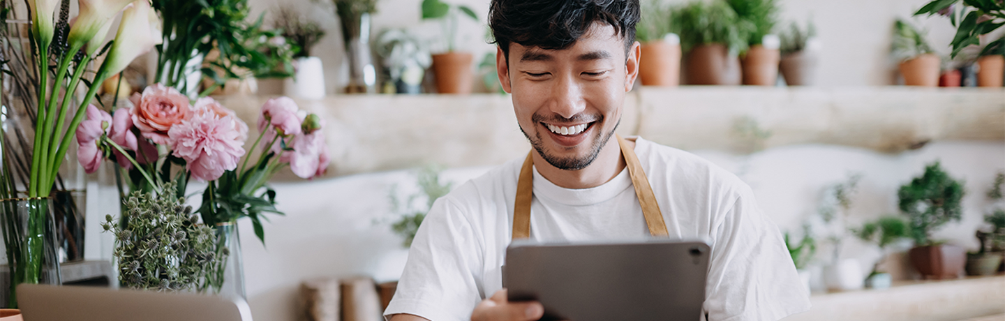 Man surrounded by flowers smiling at tablet