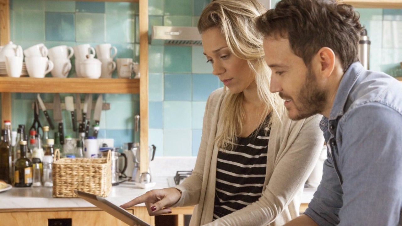 A man and a woman look at a tablet in a kitchen. 