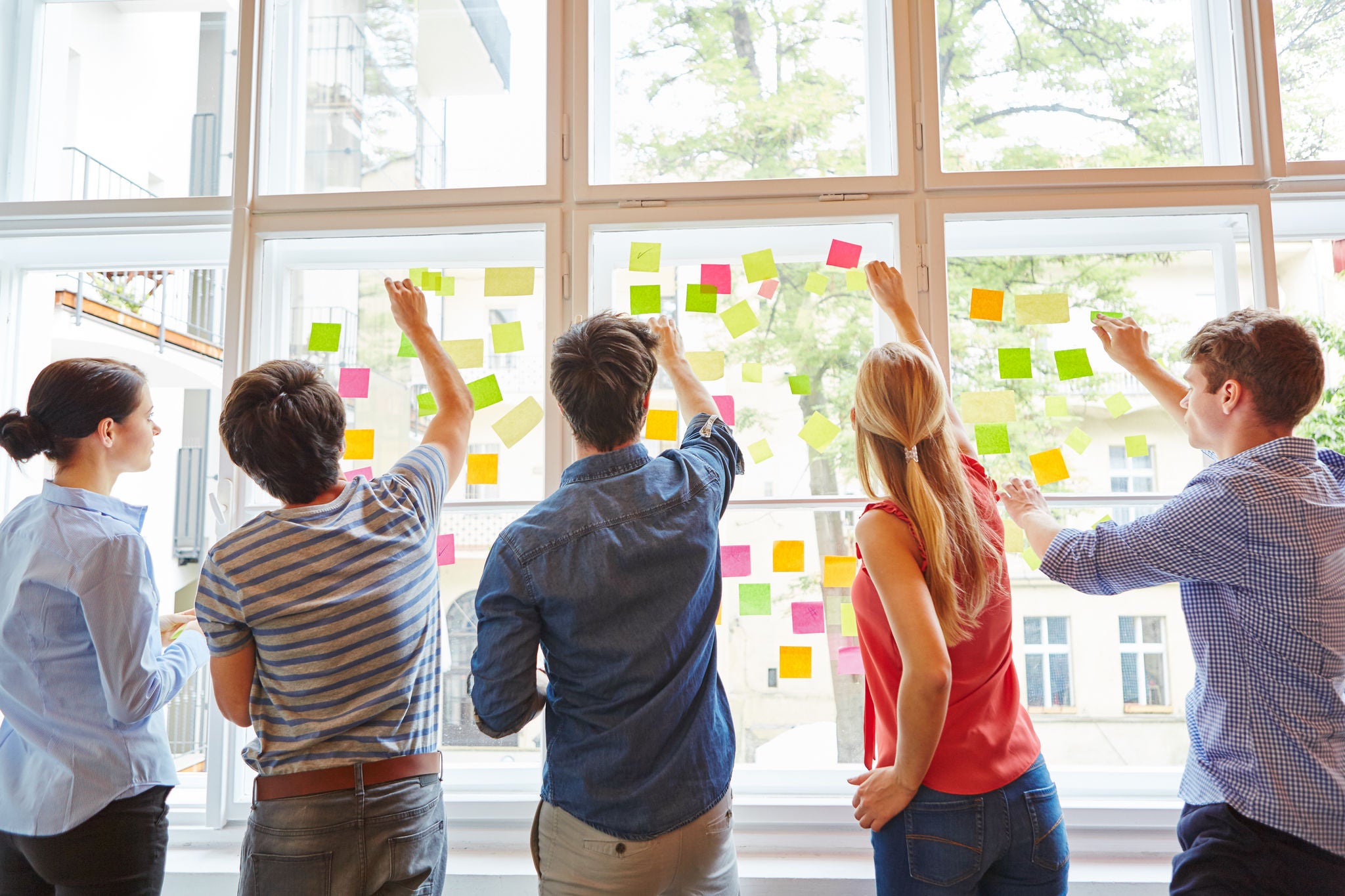 Students brainstorming by placing post-it notes on a window.
