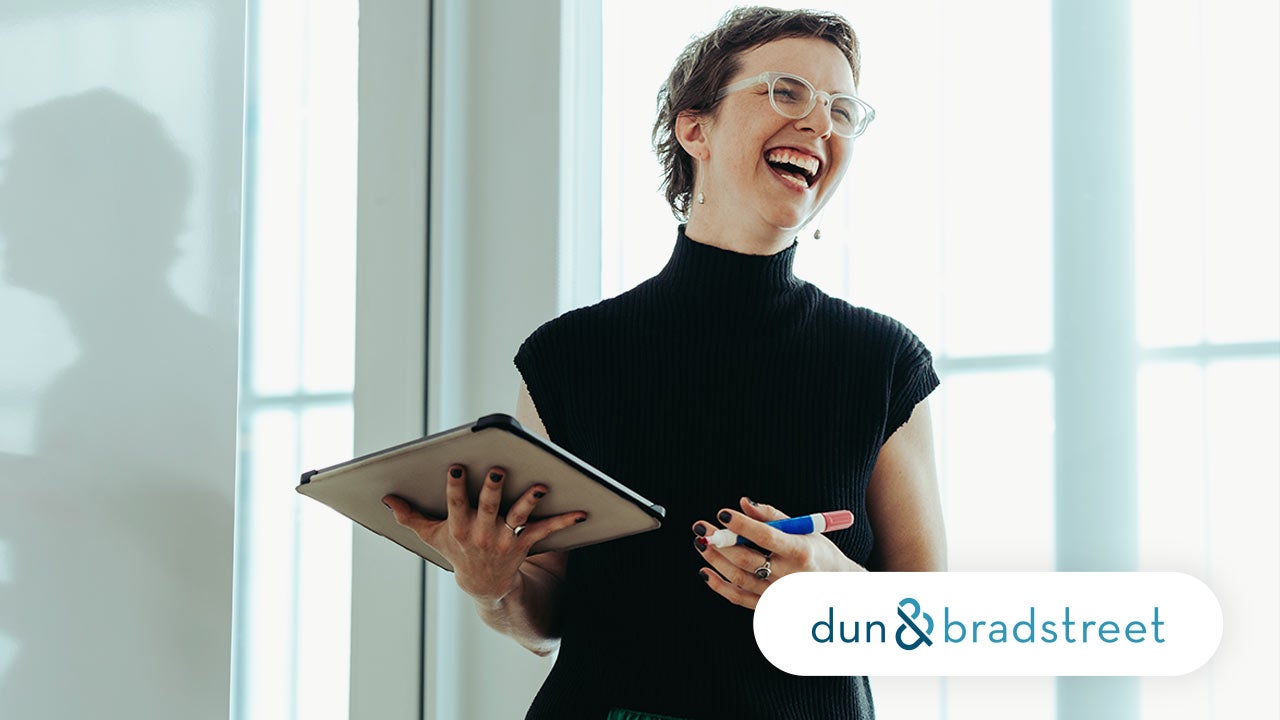 Laughing woman standing in office with a tablet. Dun & Bradstreet logo.