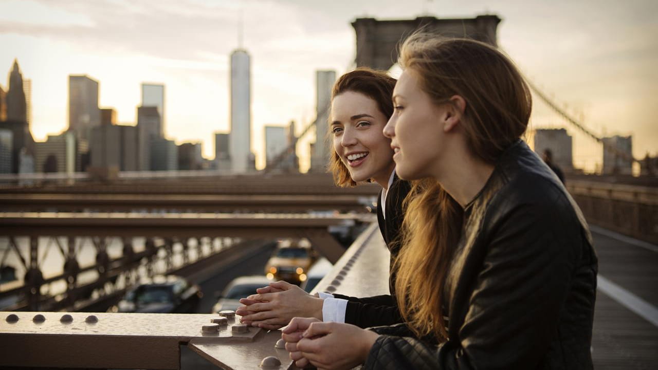 two women smiling near a city bridge