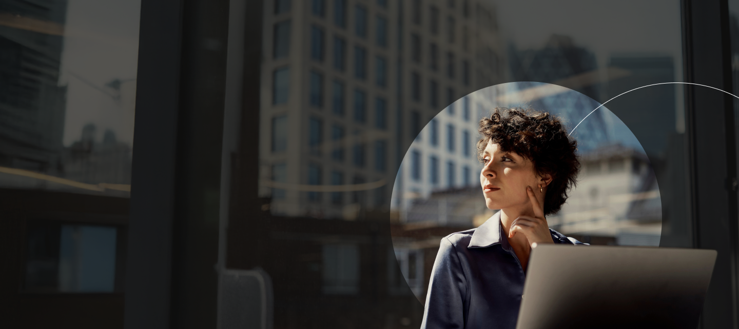Woman in office looking out into the distance with laptop infront of her