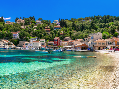 A picturesque European coastal town with clear turquoise water and hillside villas, a popular destination for summer travelers.