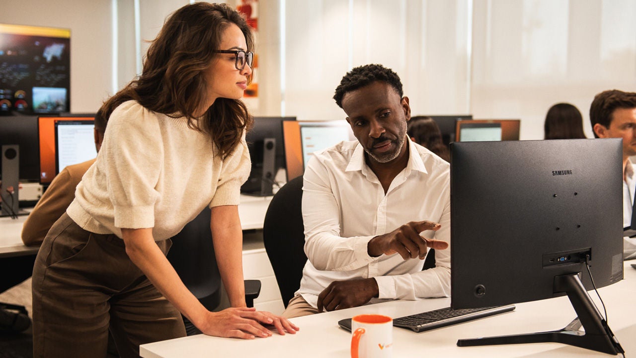 Woman assisting man with data on desktop computer