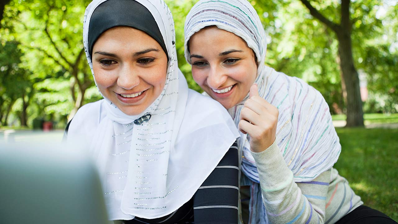 Deux femmes, portant le hijab, travaillant sur un ordinateur portable à l'extérieur.