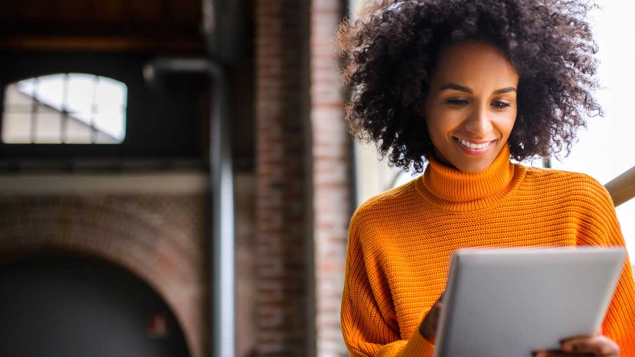En kvinde med stort, krøllet hår smiler, mens hun kigger på en tablet.