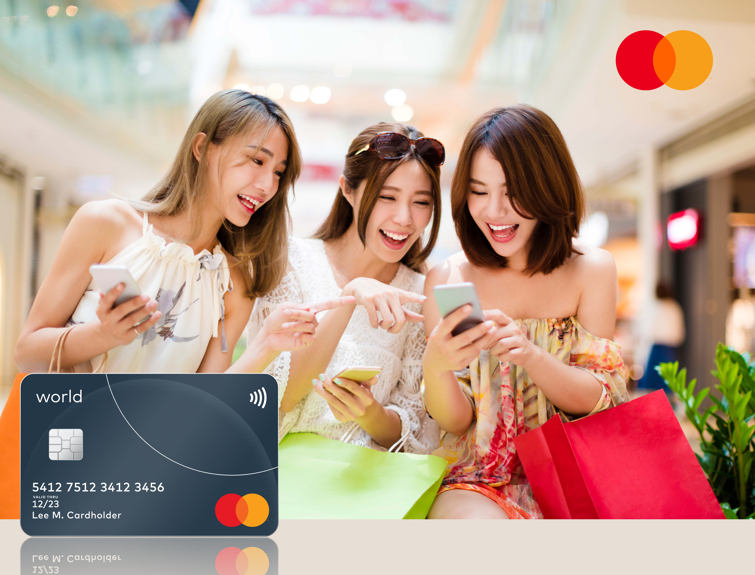 Three young women look at their phones together and laugh in a shopping mall, holding shopping bags, with a dark payment card shown in the lower left.