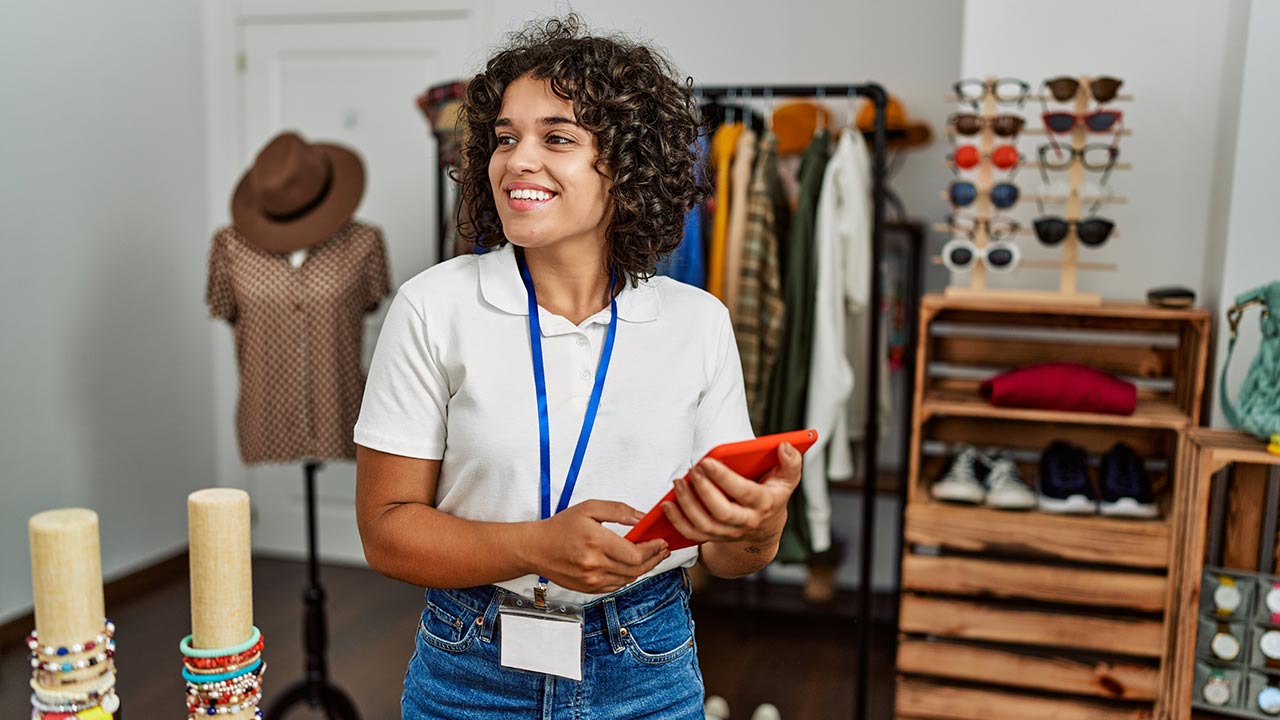 Female shopkeeper using touchpad, working at clothing store.