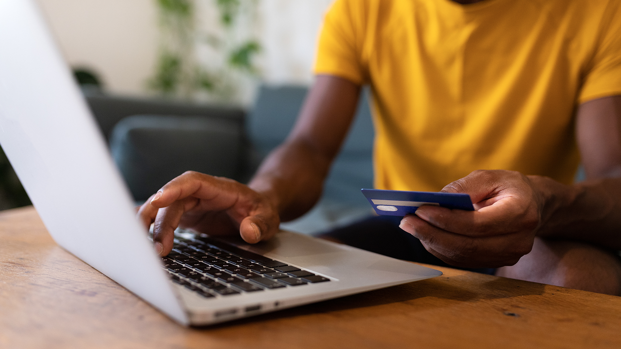 A man sitting at a table with a laptop and a credit card 