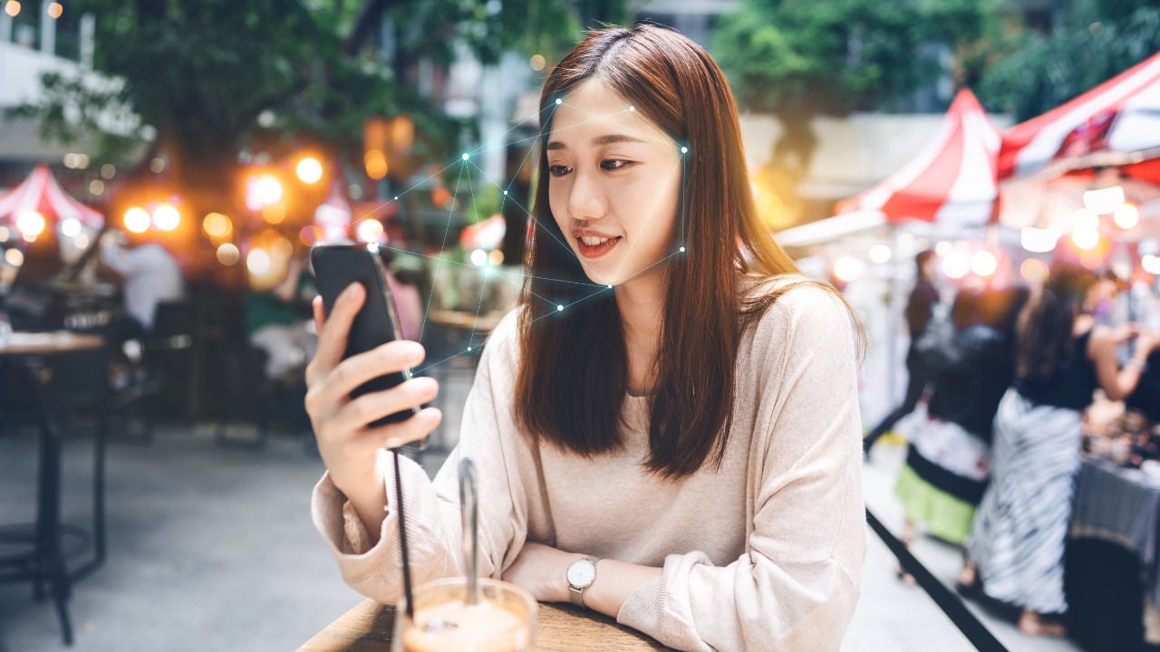 A woman sitting outside looks at her camera for authentication.