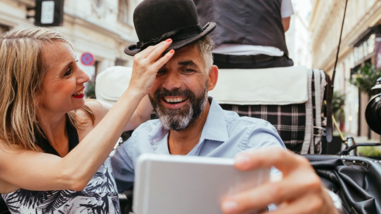 Femme mettant un chapeau melon à son compagnon lors d'une promenade en calèche, illustrant l'impact de l'inflation sur les dépenses de consommation et l'endurance de l'économie de l'expérience.
