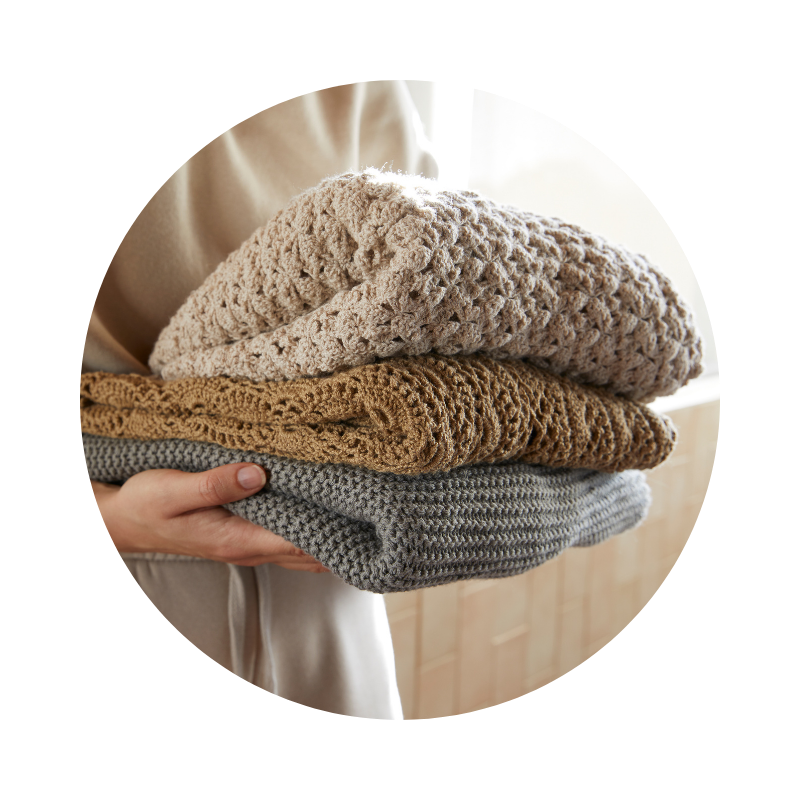 Kézben tartott, egymásra hajtogatott kötött ruhák természetes színekben, puha és fenntartható textíliákat hangsúlyozva.