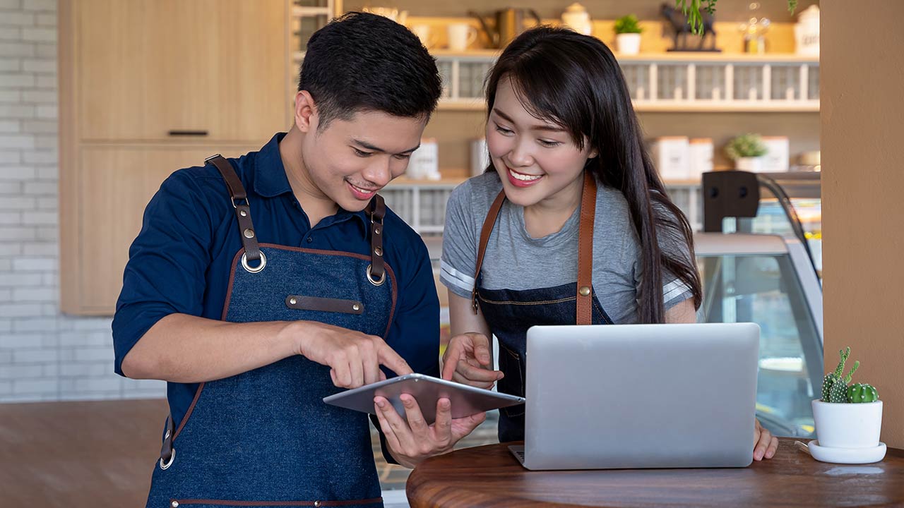 Two shop owners working on laptop at the counter of a shop.