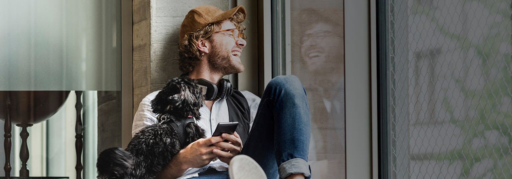 Homme avec chien et téléphone à la main regardant par la fenêtre