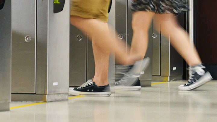 Emberek lábai mozgás közben beléptetőkapuk mellett, beltéri közlekedőtérben