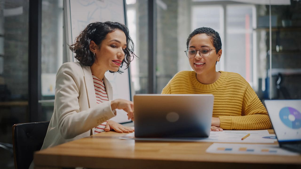 Two women sitting at a table with a laptop 