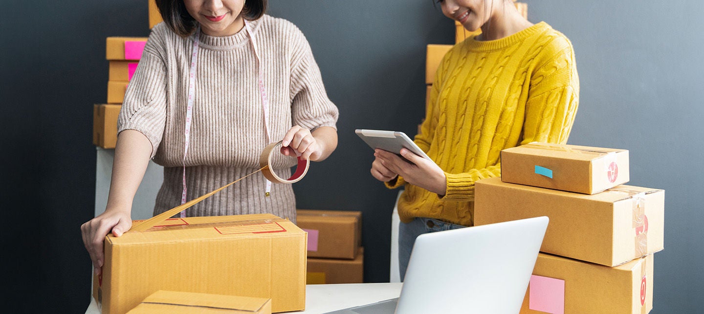 Frauen packen gemeinsam Kartons für den Versand