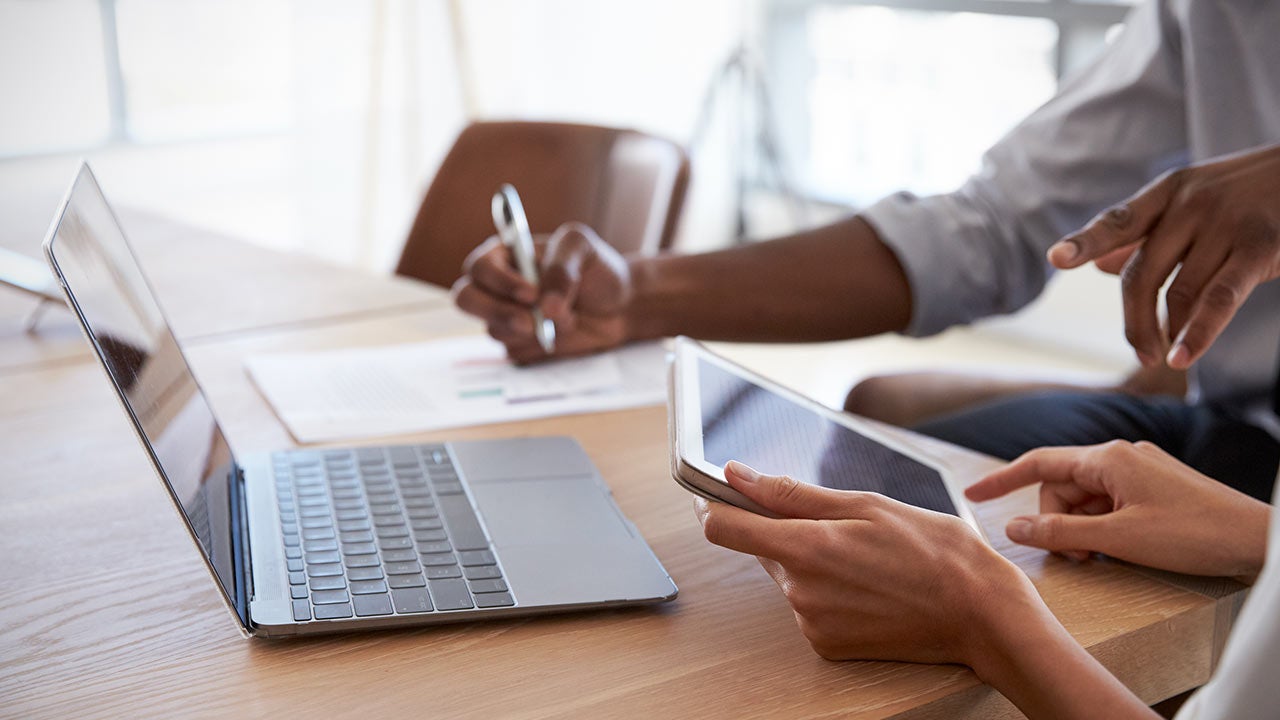 Close up of 2 people's hands working on different devices in boardroom.
