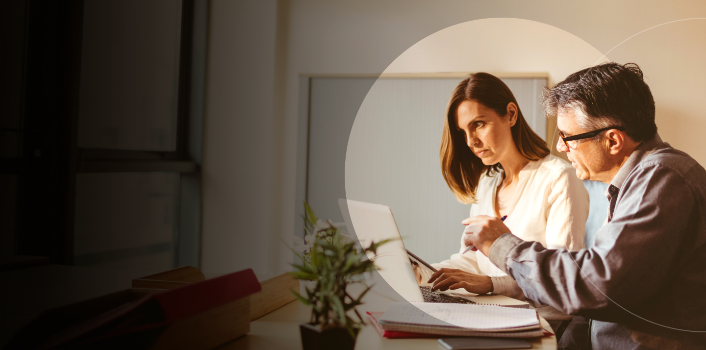 Two business professionals, a man and a woman, collaborating and discussing a project on a laptop in an office. 