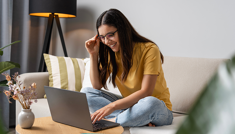Frau lächelt auf dem Sofa und schaut auf ihren Laptop