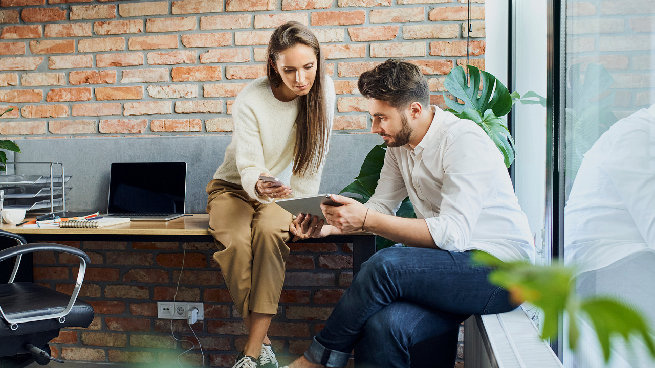 A man and woman sitting down looking at a tablet and phone