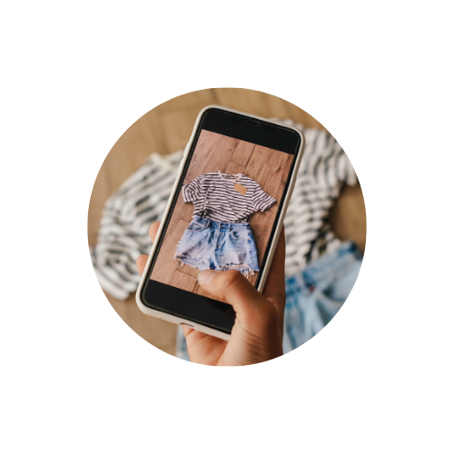 Kézben tartott okostelefonon ruhaszett fotója (csíkos felső és farmer rövidnadrág), divat- és online vásárlási koncepció, kör alakú kivágásban.”