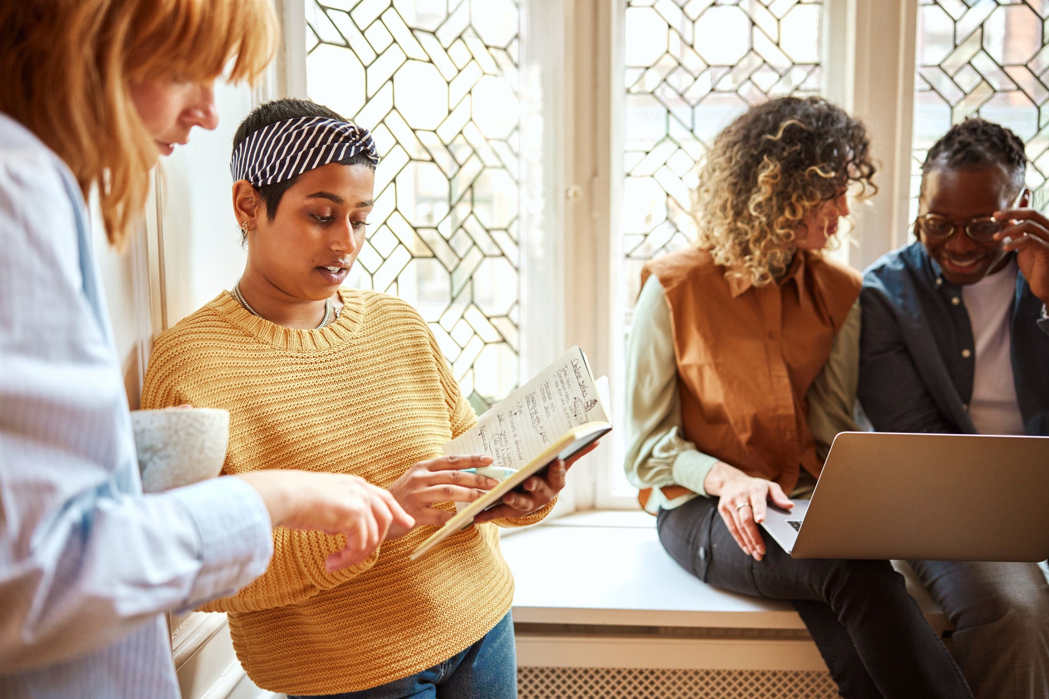 Two diverse young businesswomen going over notes together during a casual meeting by a window in a modern office