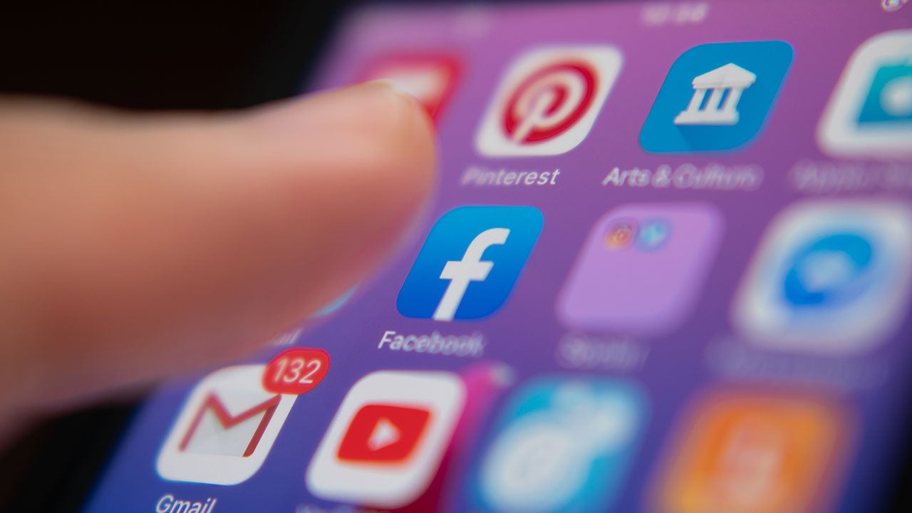 User touching Facebook logo on a phone screen.