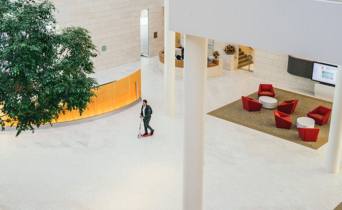 En mann på en elsparkesykkel inne i en stor kontorlobby.