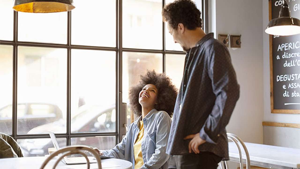 En kvinde og en mand sidder på en café og griner sammen.