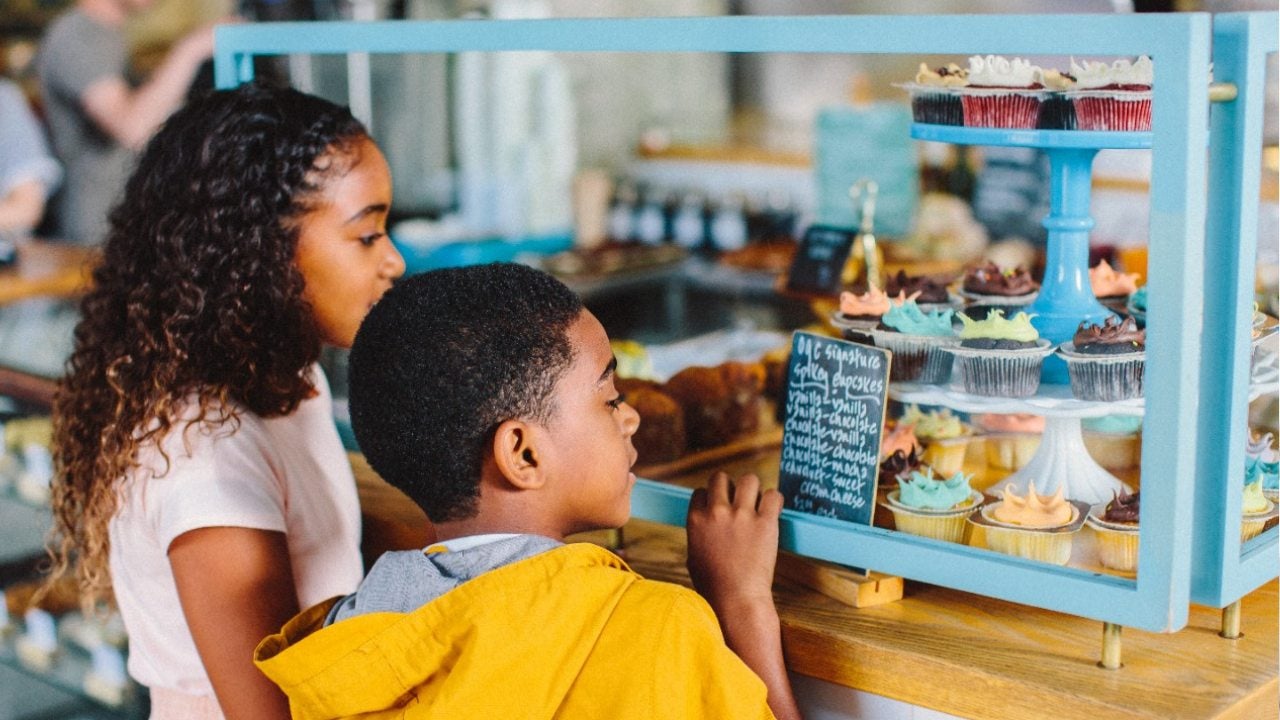 Two kids look at a display in a bakery. 
