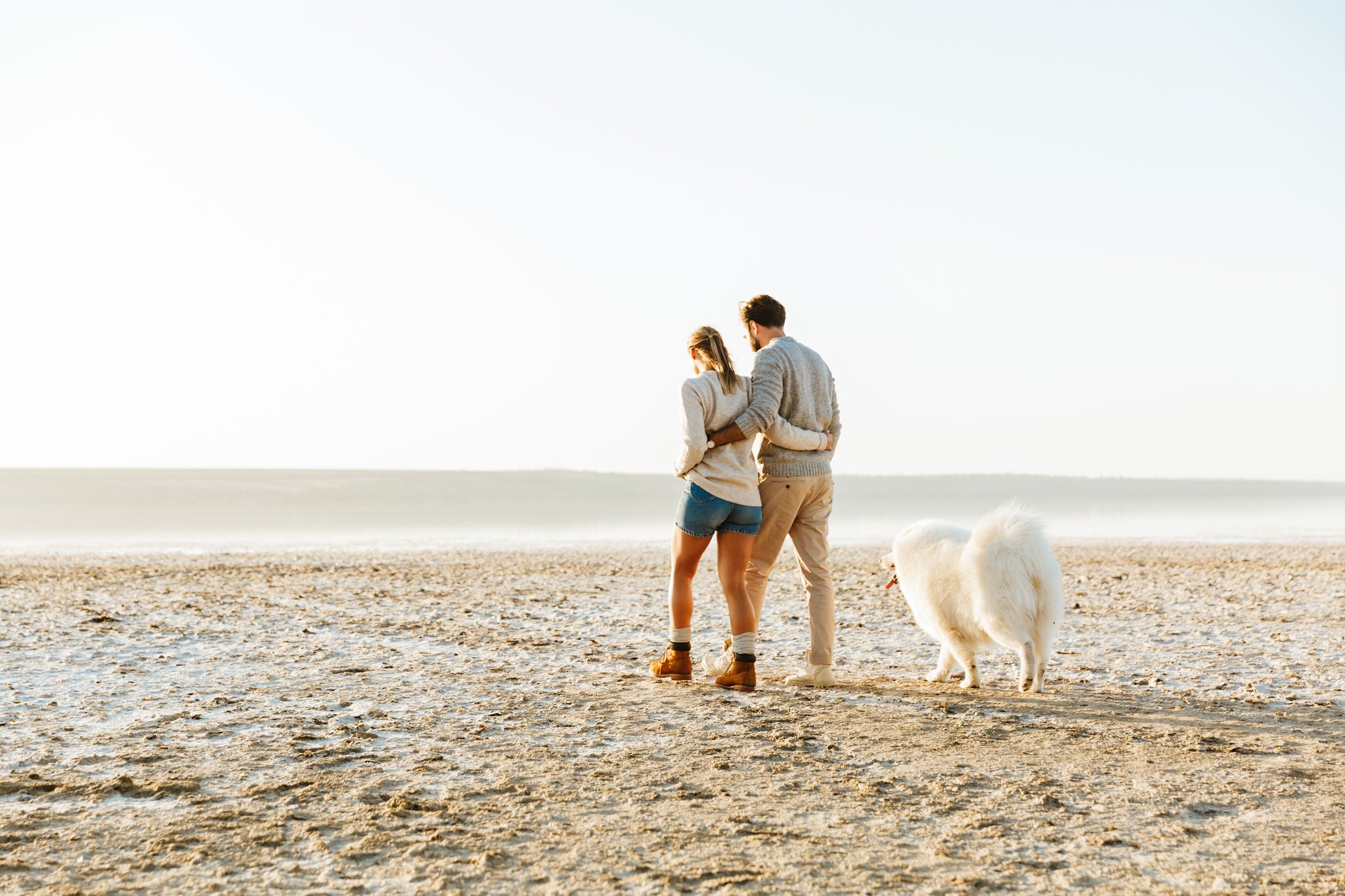 Mladi par šeta plažom sa psom. 