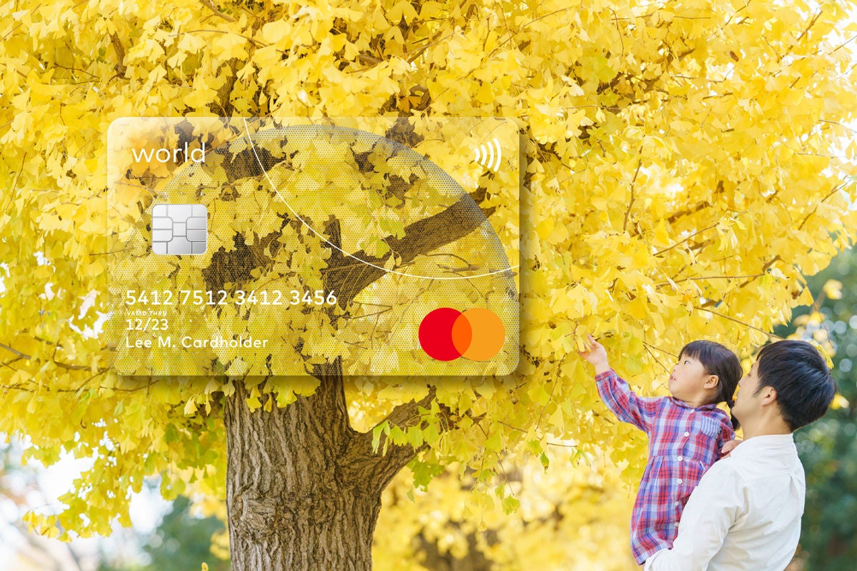 A man holds a young child up towards the branches of a golden ginkgo tree, with a payment card shown above them.