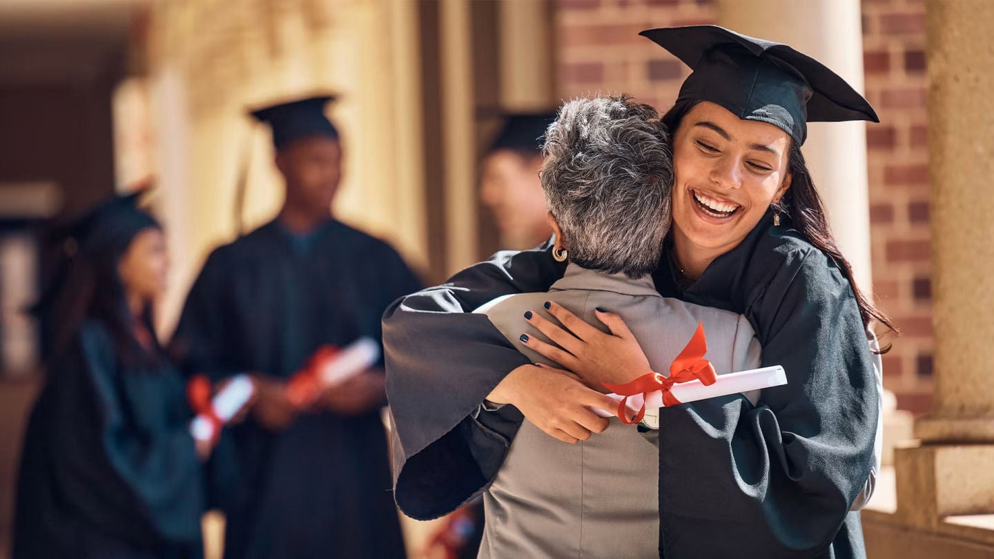Mulher sorridente a formar-se na escola e a abraçar outra pessoa.