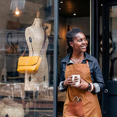 small business owner standing in front of store holding a coffee mug.