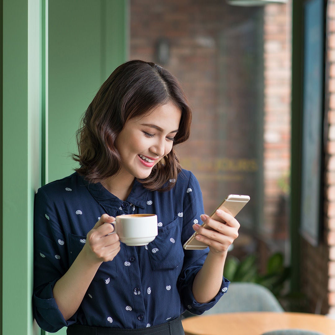 Girl in Blue dress looking into mobile while having a coffee.