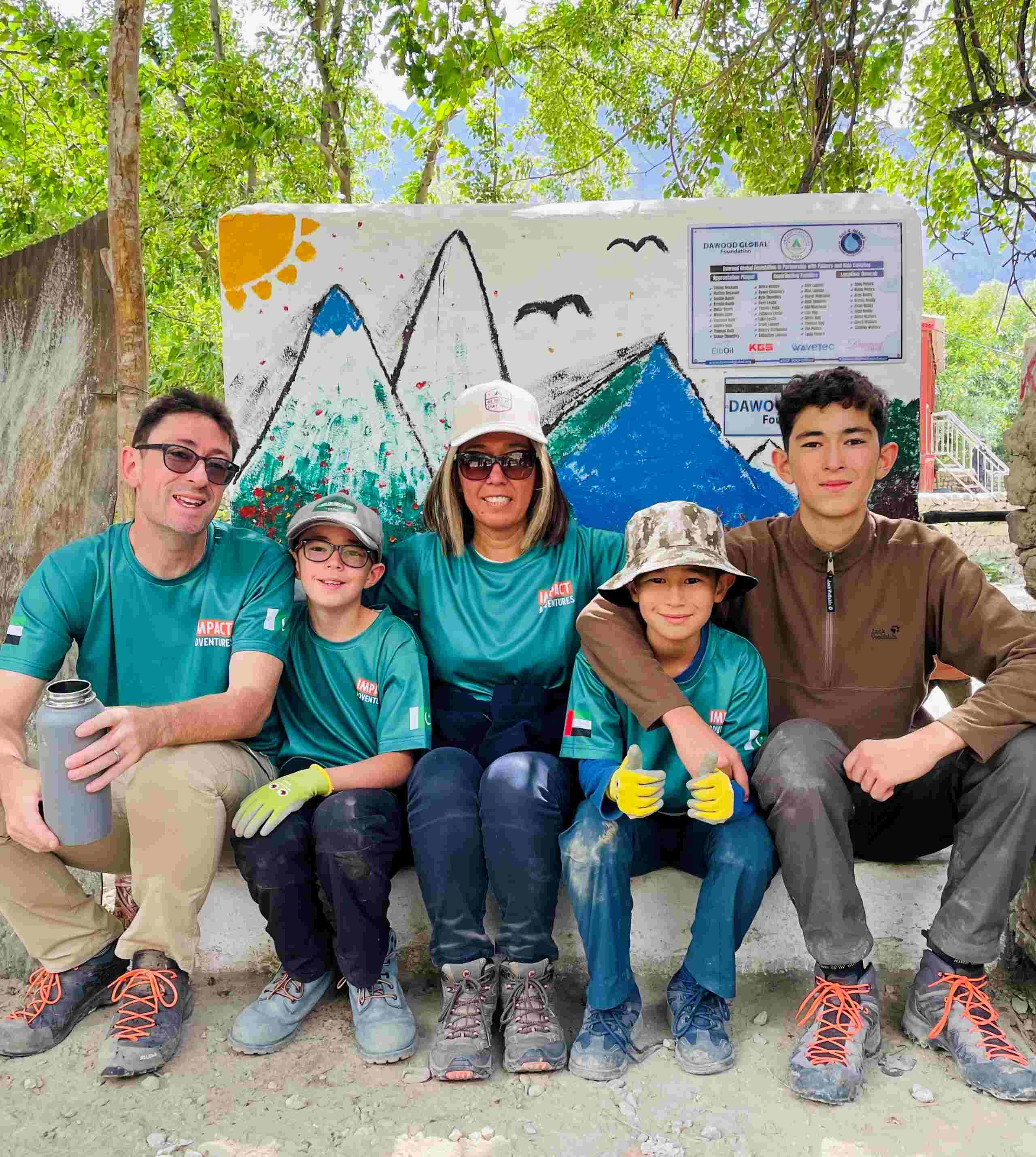 Kuntay Simbatova and her family sit in front of a painted sign about her water project in Pakistan. 