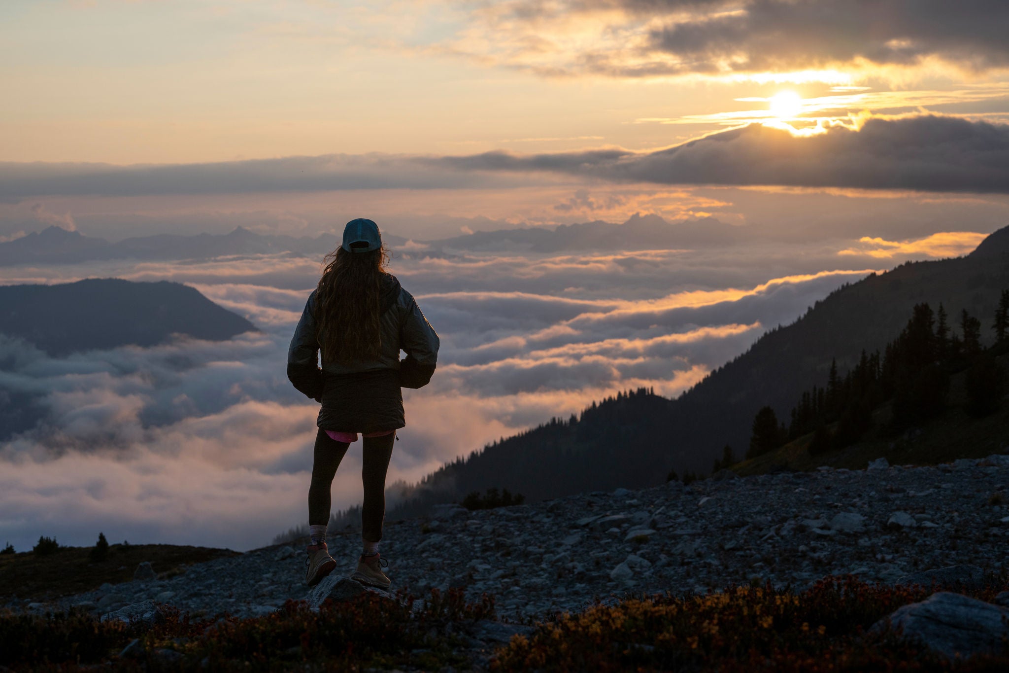 Young Woman Looks Over Cloudscape From Mountain Top