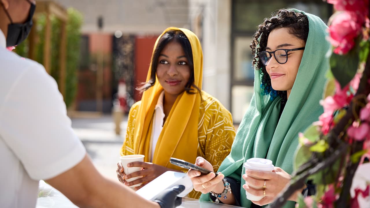 Deux femmes portant un foulard achetant du café via le paiement mobile