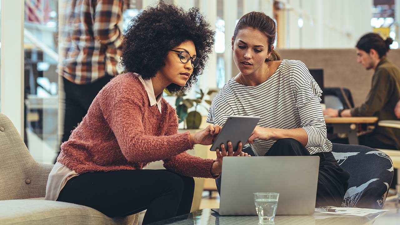 Female coworkers discussing work in a modern office.