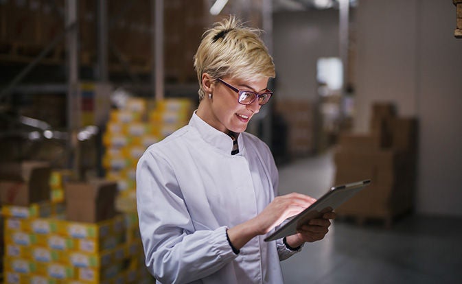 Happy caucasian female worker using tablet in warehouse.
