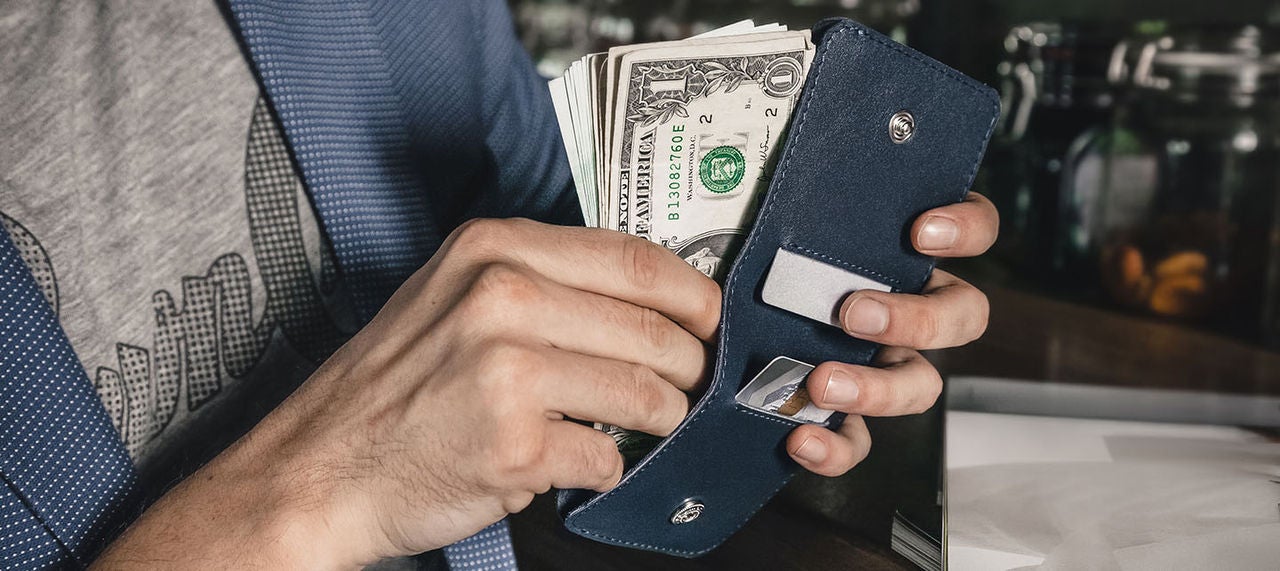 Close-up of man’s hands pulling dollar bills from a wallet at a counter.