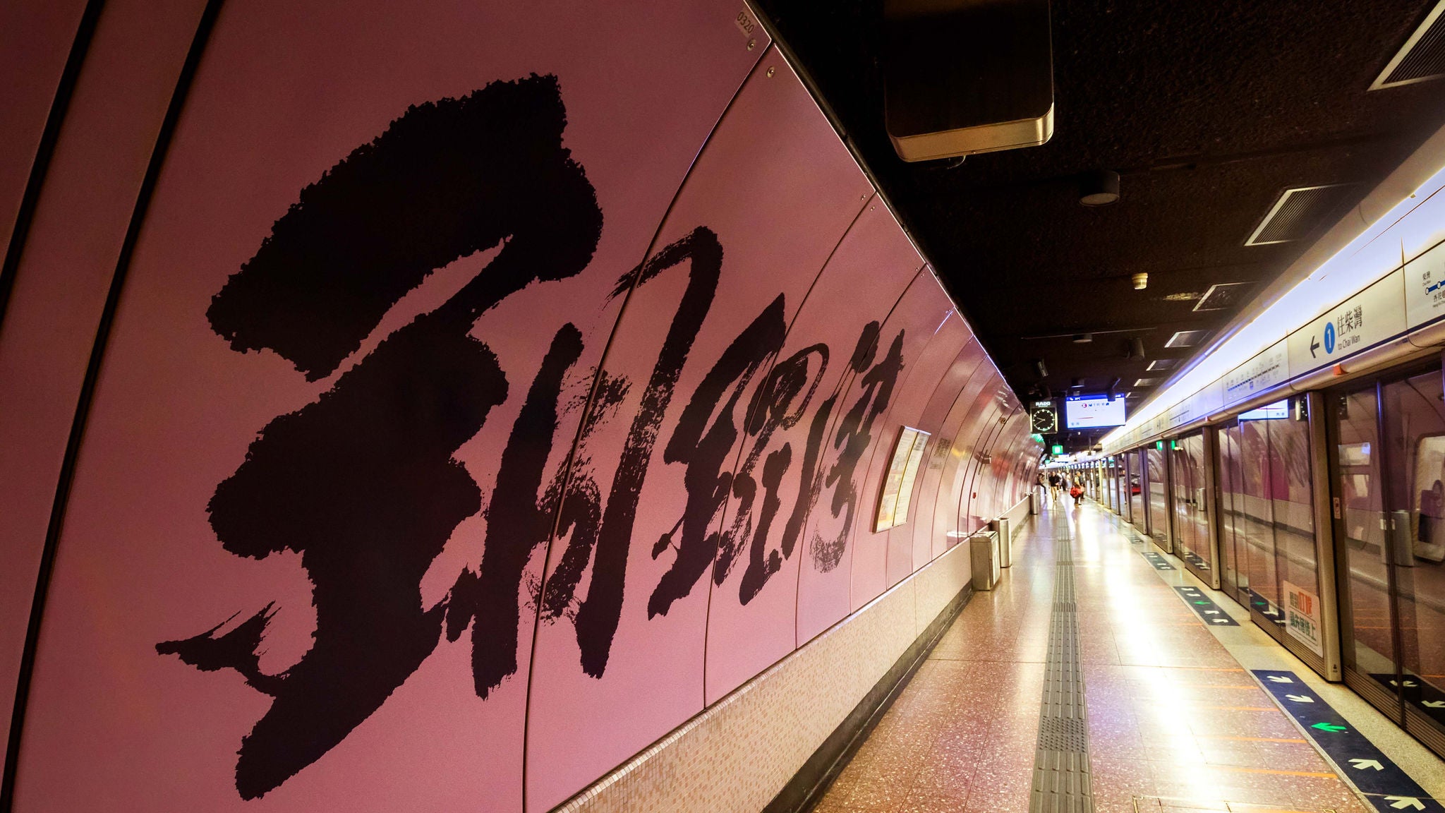 An underground metro platform with large brush-stroke Chinese calligraphy painted across a pink curved wall.