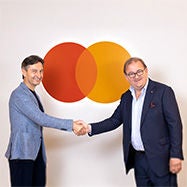 Two men shaking hands in front of a Mastercard logo, symbolizing partnership and collaboration.