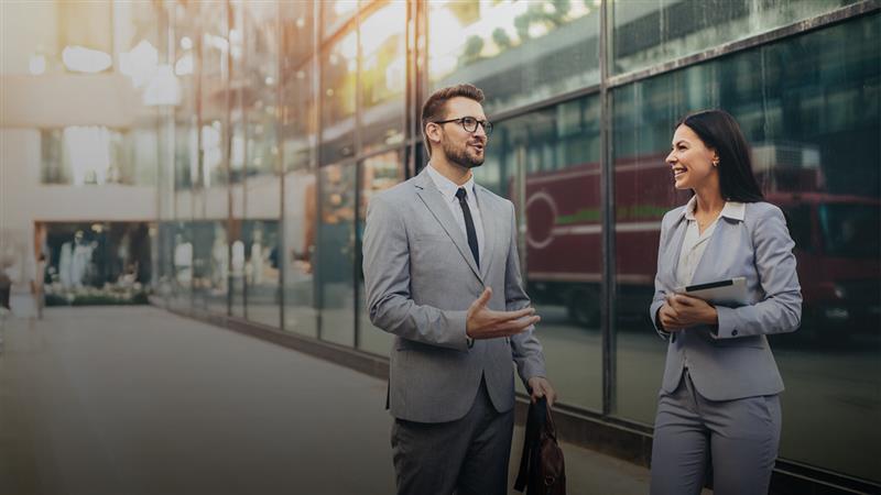 Professional woman and man talking on sidewalk.