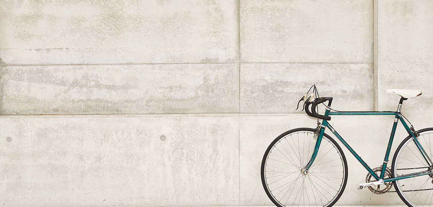 Grønn landeveissykkel med hvitt sete lent mot en lys betongvegg.