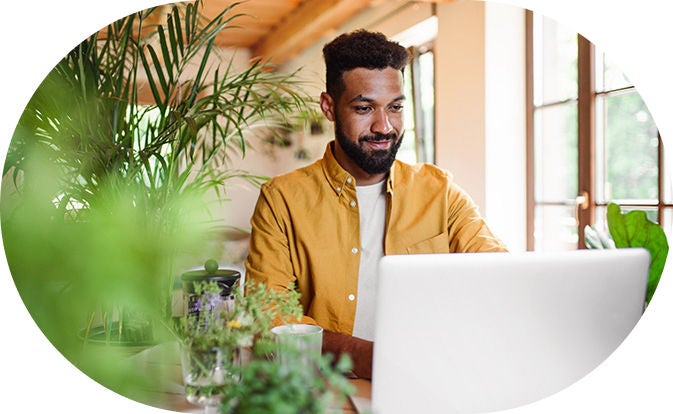 A man smiling while working on his laptop in a bright and modern environment.