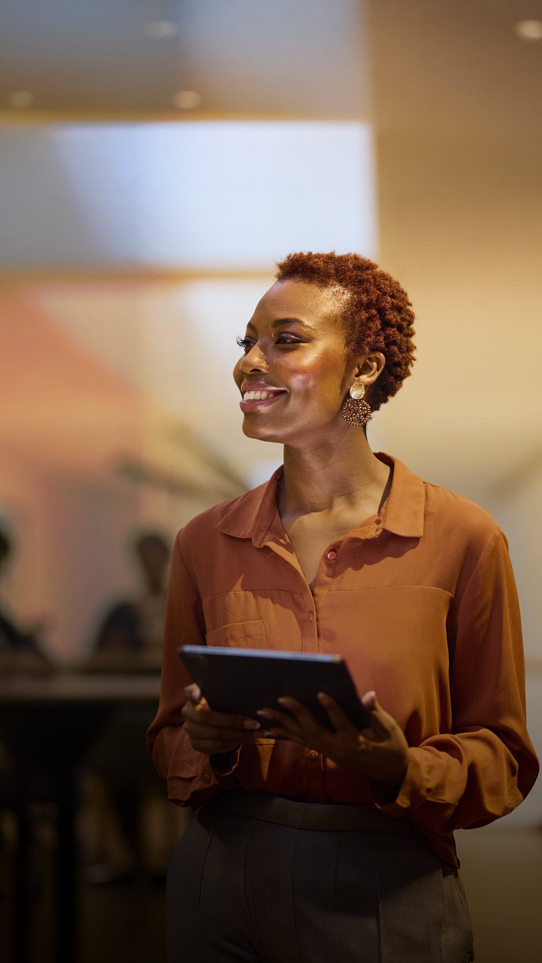 A woman standing in her living room smiles at her phone. 