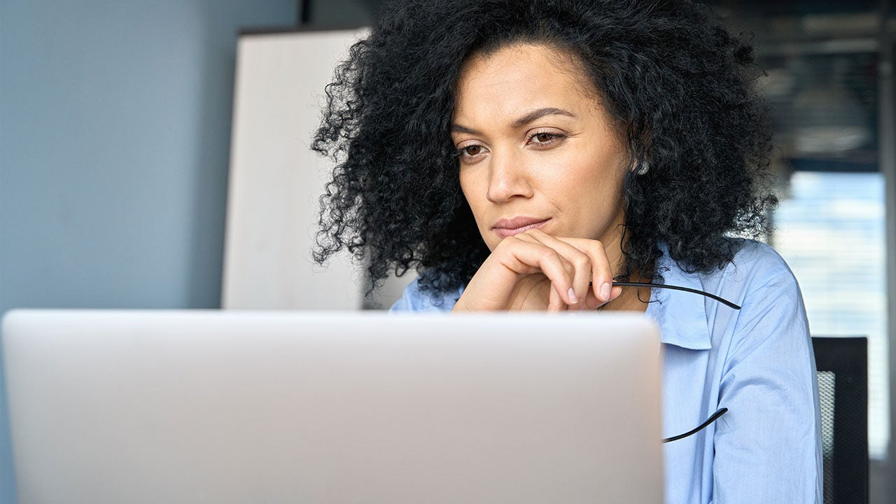 Serious businesswoman sitting at a desk, looking at laptop.